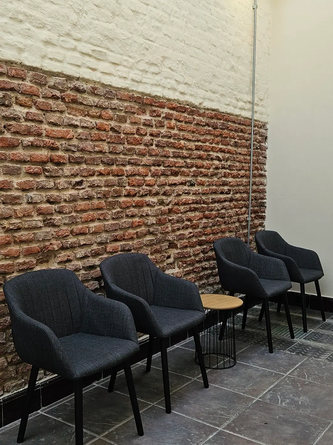 Sala de espera de Espacio 1010 con cuatro butacas tapizadas oscuras y mesa auxiliar frente a un muro de ladrillo a la vista