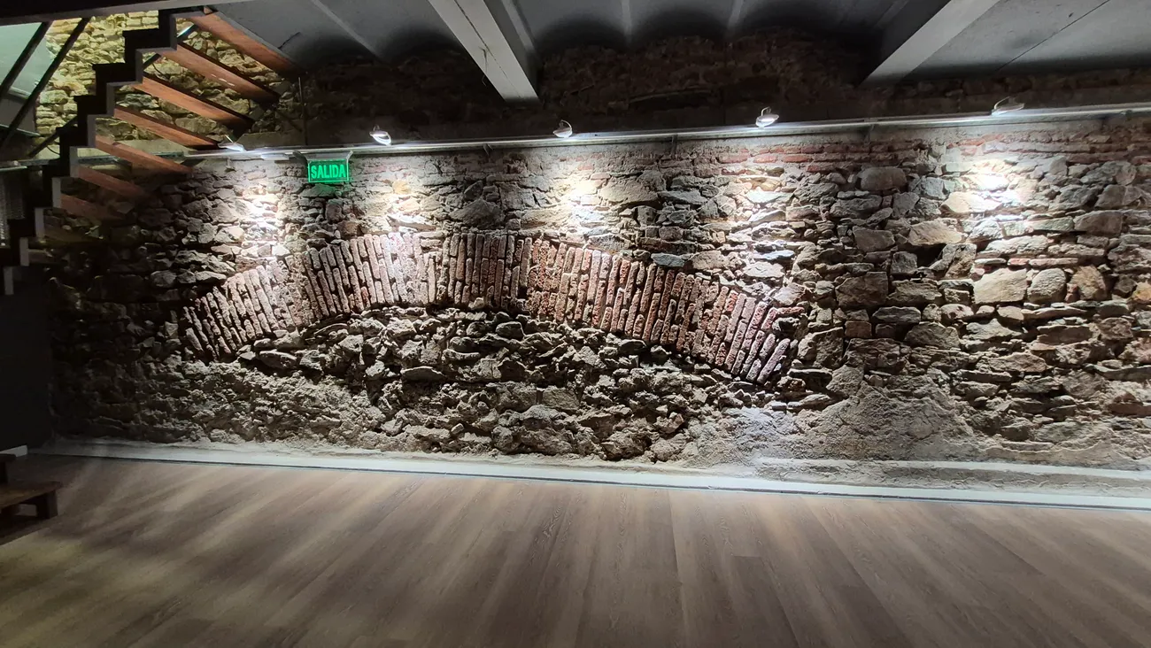 Subsuelo de Espacio 1010 con muro de piedra y arco original iluminado, piso de madera